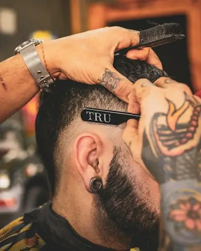 Barbeiro acertando o corte de um cliente com navalha
