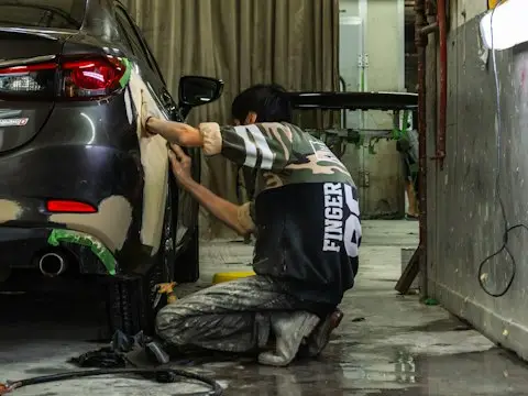 Uma pessoa lixando a traseira de um carro cinza